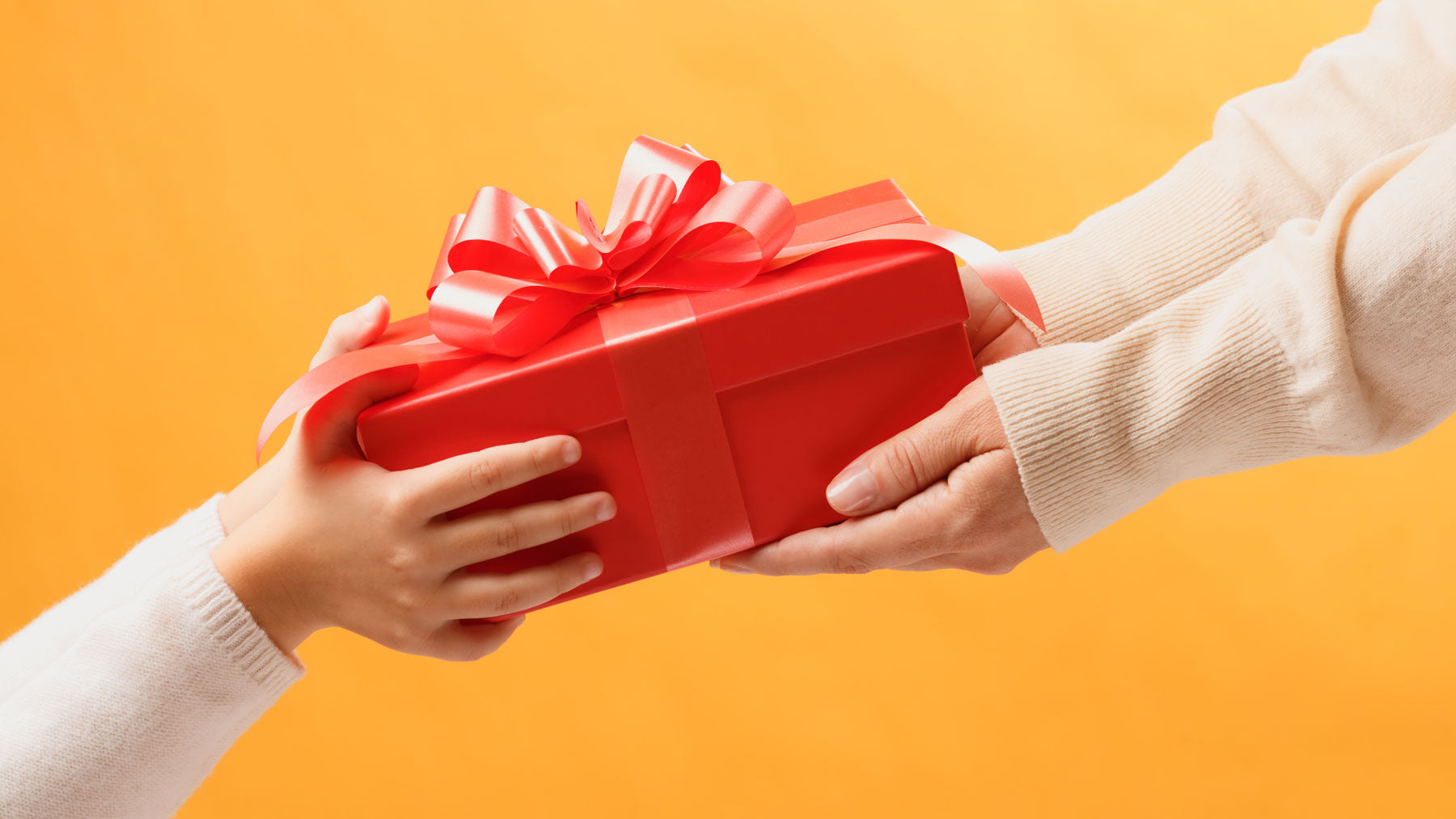 Hands passing a red Taffy Town gift box, a candy gift idea for birthdays, thank yous, and just because surprises.