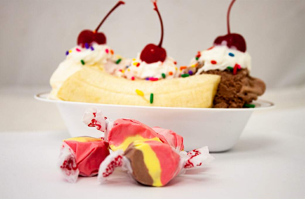 Taffy Town banana split salt water taffy candy inspired by the classic dessert, shown in front of banana split sundae
