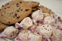 A plate of soft chocolate chip cookies surrounded by Taffy Town’s Chocolate Chip Cookie taffy candy—gourmet salt water taffy with real chocolate bits and nostalgic flavor.