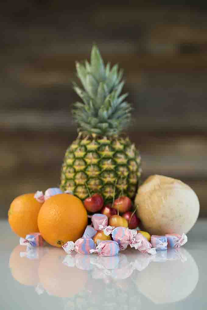 A colorful mix of Tropical Punch taffy candy from Taffy Town placed with fresh pineapple, oranges, cherries, and coconut—gourmet salt water taffy inspired by tropical flavors.